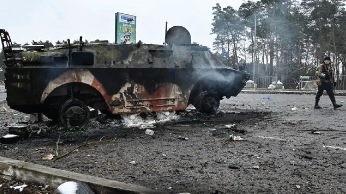 أوكراني مسلح يسير أمام ناقلة جنود روسية محترقة على نقطة تفتيش في مدينة بروفاري خارج كييف في 1 مارس 2022