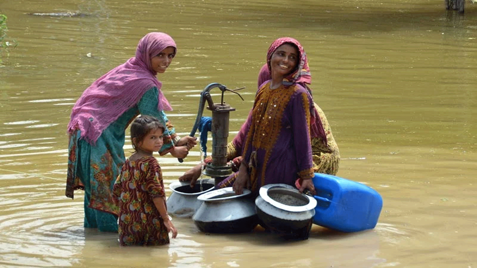 نساء متضررات من الفيضانات يملأن مياه الشرب من مضخة يدوية وسط شارع غمرته الفيضانات بعد هطول أمطار موسمية غزيرة في منطقة جعفر أباد في إقليم بلوشستان في 29 آب\ أغسطس 2022.