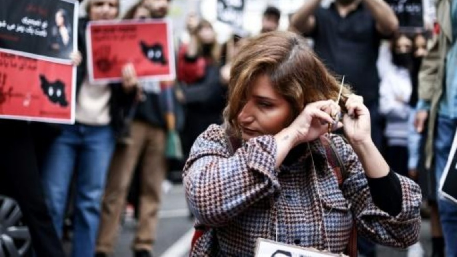 امرأة تقص شعرها تضامناً مع مهسا أميني أمام مبنى السفارة الإيرانية في بروكسل في 23 سبتمبر 2022 
