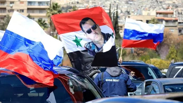 سوريون يلوحون بالعلم الروسي وصورة بشار الأسد خلال مسيرة تأييد لروسيا في غزوها أوكرانيا في 25 مارس 2022
