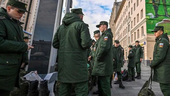 جنود روس ينتظرون رحيلهم وهم يقفون بالقرب من لوحة جدارية تصور جنودًا روس يرتدون شارات ذراع رمز Z في وسط موسكو، في 16 أكتوبر 2022