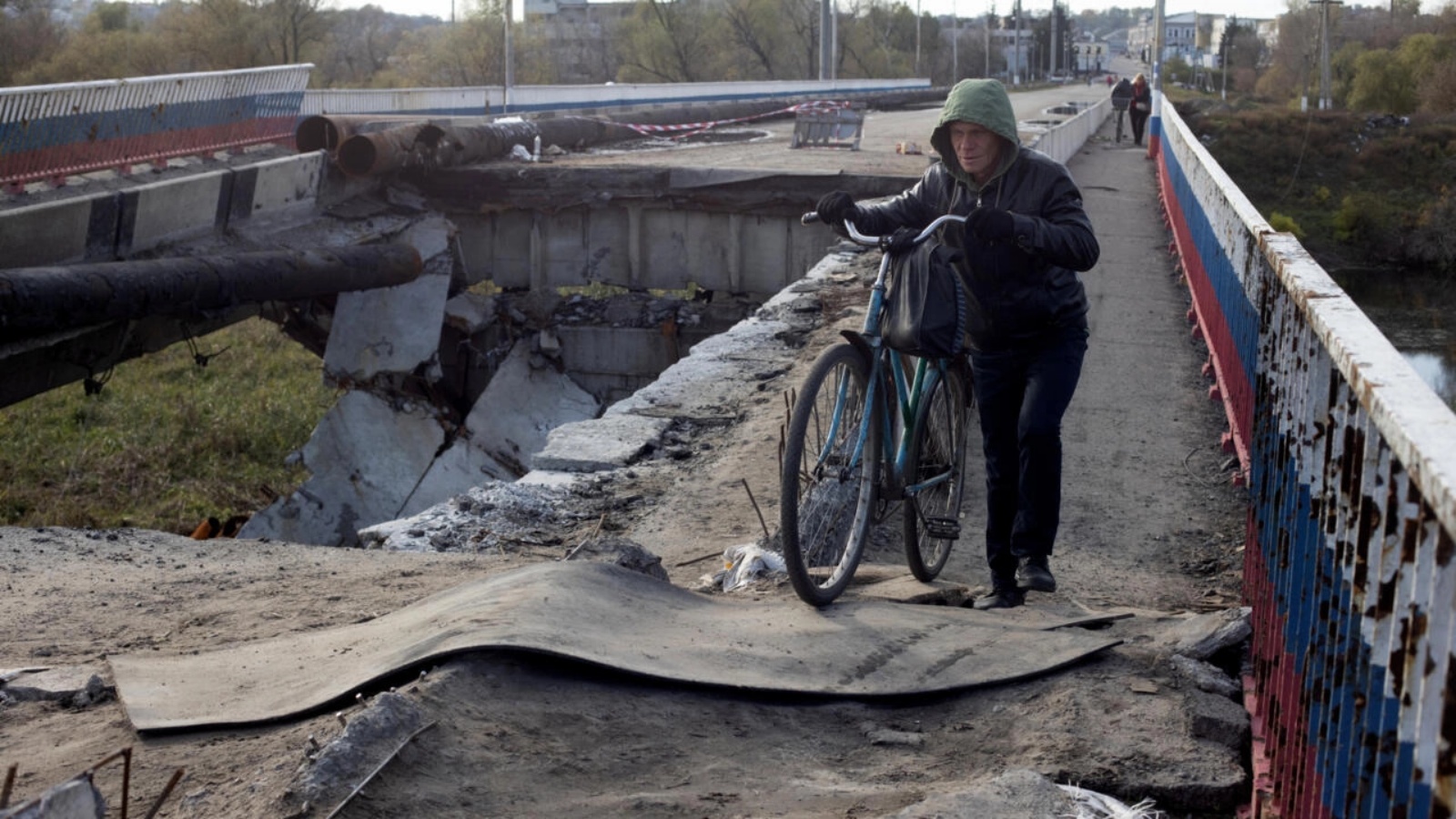 رجل يدفع دراجته على جسر مدمّر بالقرب من بوريفسك، في منطقة خاركيف في 23 أكتوبر 2022