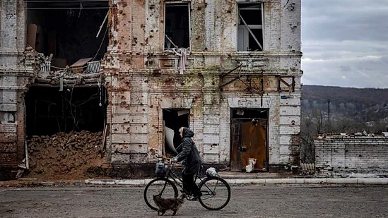أوكرانية تركب دراجة هوائية أمام مبنى متضرر في بلدة كوبيانسك