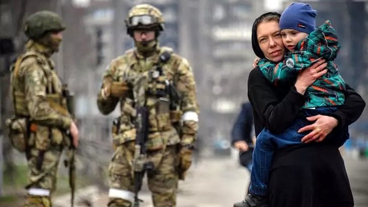 امرأة وطفلها يسيران أمام جنود روس في ماريوبول، جنوب شرق أوكرانيا