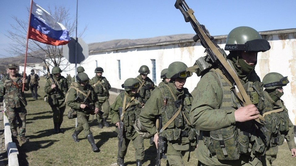 رجل يحمل العلم الروسي يحيي مسلحين يرتدون زيا عسكريا يمنعون الوصول إلى قاعدة لحرس الحدود الأوكراني ليست بعيدة عن قرية بيريفالن بالقرب من سيمفيروبول في 3 مارس/آذار 2014