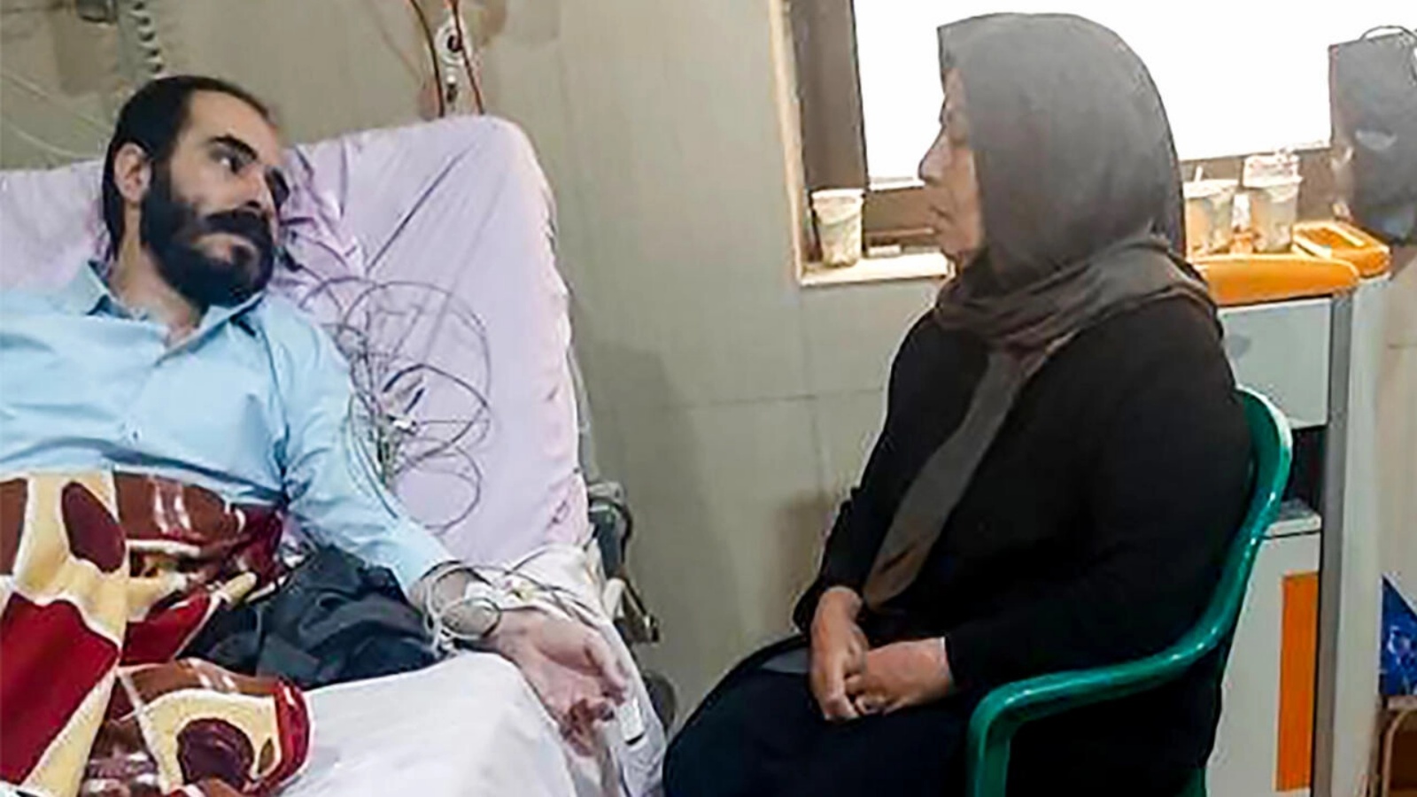 صورة وزعها المركز الإعلامي التابع للسطة القضاء في إيران تظهر حسين رونقي في المستشفى بينما تجلس والدته بجانبه في طهران بتاريخ 14 نوفمبر 2022