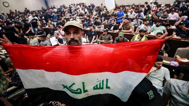 متظاهر يرفع العلم الوطني بينما يتجمع أنصار رجل الدين العراقي مقتدى الصدر داخل البرلمان العراقي في المنطقة الخضراء شديدة الحراسة بالعاصمة بغداد