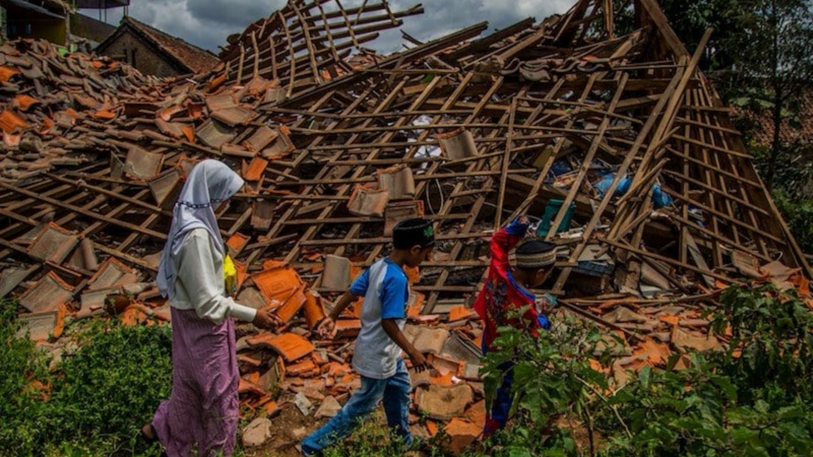 أشخاص يمرون بحطام منزل بعد زلزال ضرب قبالة إندونيسيا