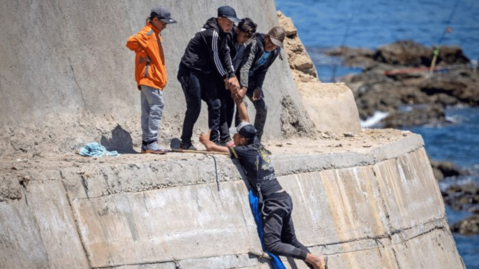 مهاجرون يتسلقون جدارًا بحريًا في مدينة الفنيدق الشمالية بعد محاولتهم عبور الحدود من المغرب إلى سبتة، جيب إسبانيا في شمال أفريقيا. في 19أيار\ مايو 2021.