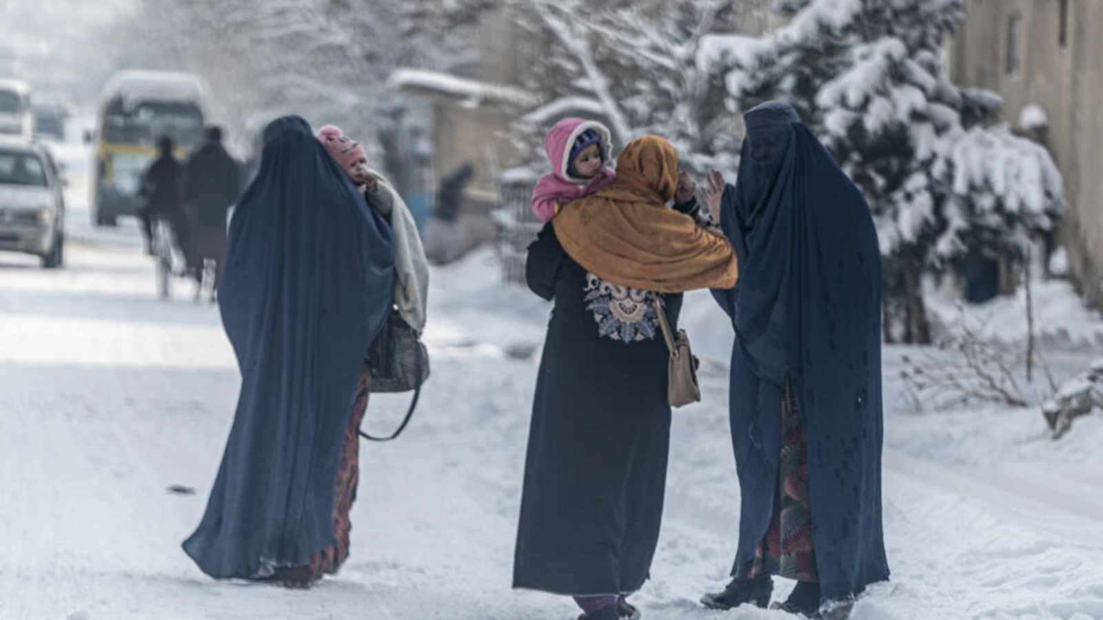 أفغانيات يحملن أطفالا يمشين في شارع مكسو بالثلج في كابول في 23 يناير 2023