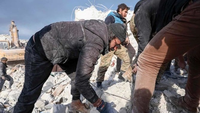 رجل سوري يساعد رجال الإنقاذ في إزالة الأنقاض بينما يبحث عن أفراد الأسرة الذين ما زالوا محاصرين تحت الأنقاض في قرية بسنايا في محافظة إدلب السورية