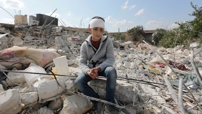 طفل سوري، فقد عائلته نتيجة الزلزال الذي ضرب تركيا وسوريا، يجلس وسط أنقاض منزل عائلته في بلدة جنديرس بحلب