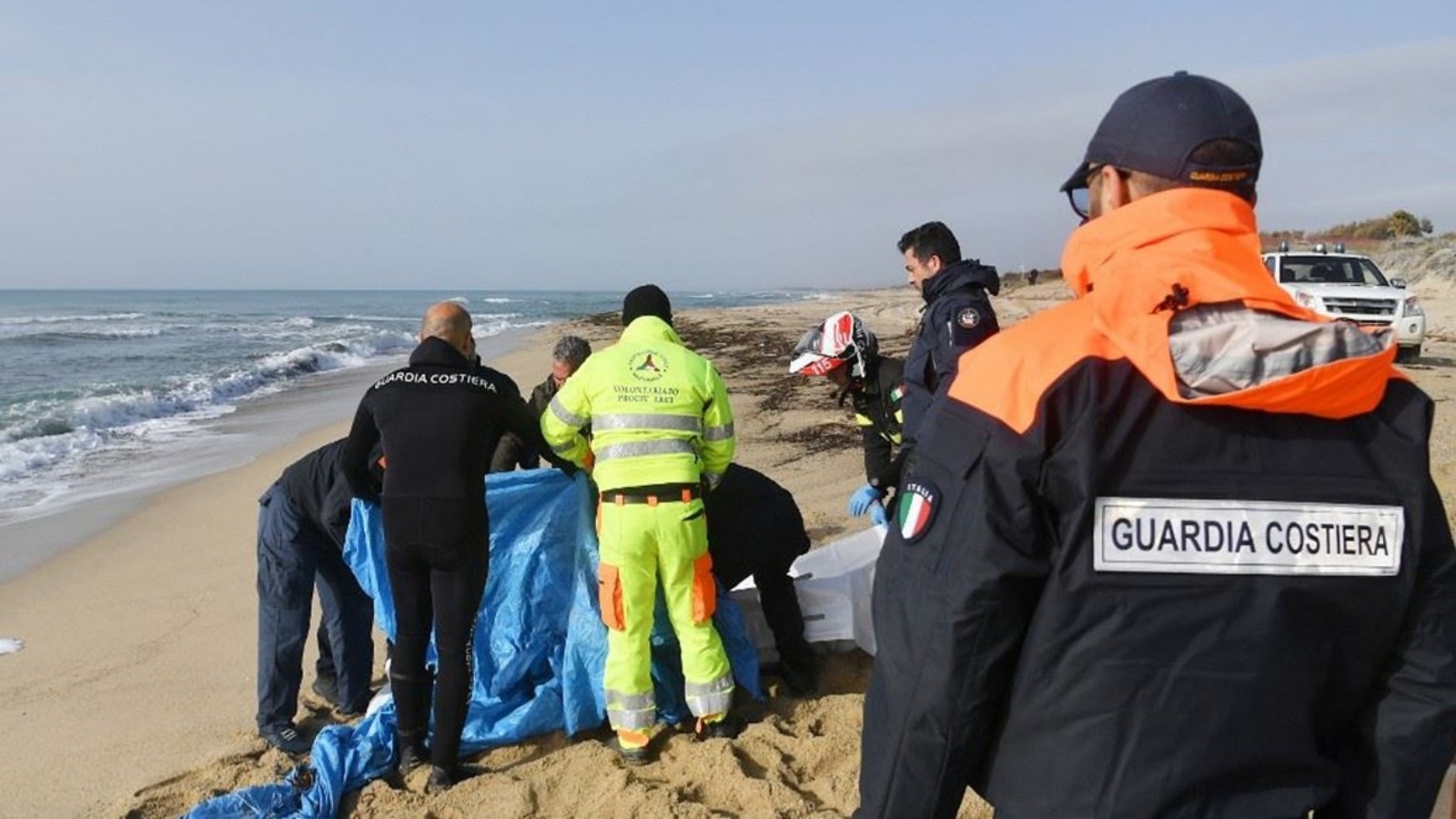 رجال الإنقاذ يقومون بتغطية جثة جرفتها الأمواج على الشاطئ بعد يومين من غرق قارب للمهاجرين قبالة منطقة كالابريا الجنوبية بإيطاليا