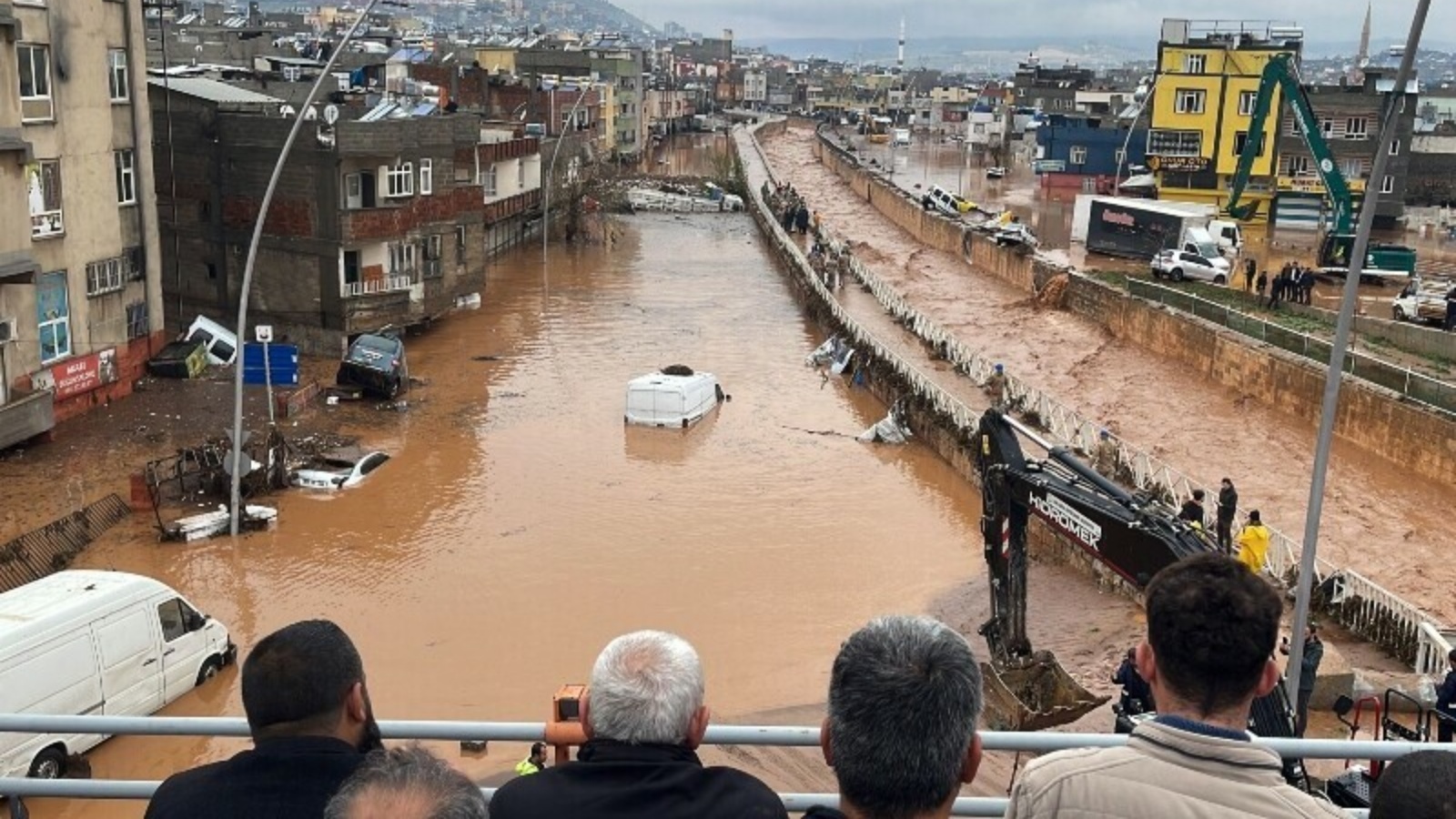 أشخاص يقفون في نقطة عالية ينظرون إلى أسفل إلى مياه الفيضانات في سانليورفا، جنوب شرق تركيا في 15 مارس