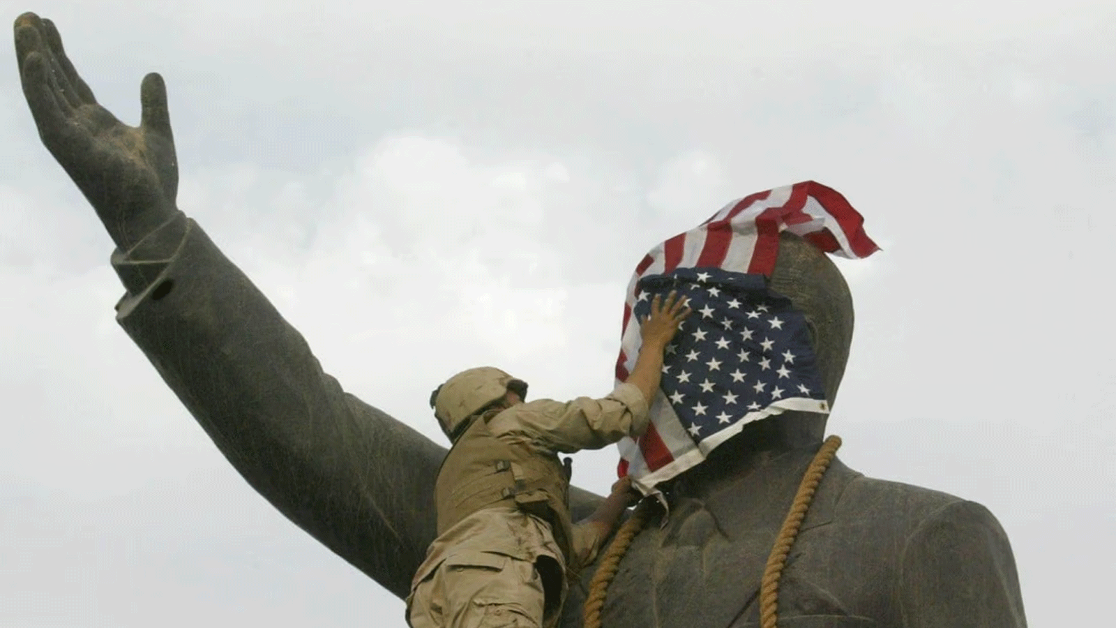 جندي من مشاة البحرية الأميركية يغطي وجه تمثال صدام حسين بعلم الولايات المتحدة في ساحة الفردوس ببغداد. 9 نيسان\أبريل 2003
