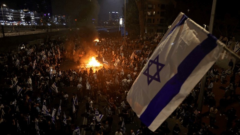 المتظاهرون يغلقون طريقا ويحملون الأعلام الإسرائيلية خلال مسيرة ضد الإصلاح القضائي للحكومة الإسرائيلية في تل أبيب، في 27 مارس 2023