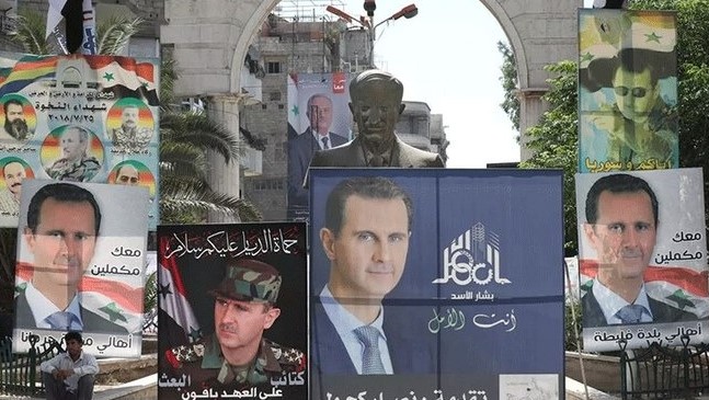 رجل يجلس بجانب تمثال الرئيس السوري الراحل حافظ الأسد، وتحيط به ملصقات لبشار الأسد، في دمشق، سوريا، 23 مايو 2021