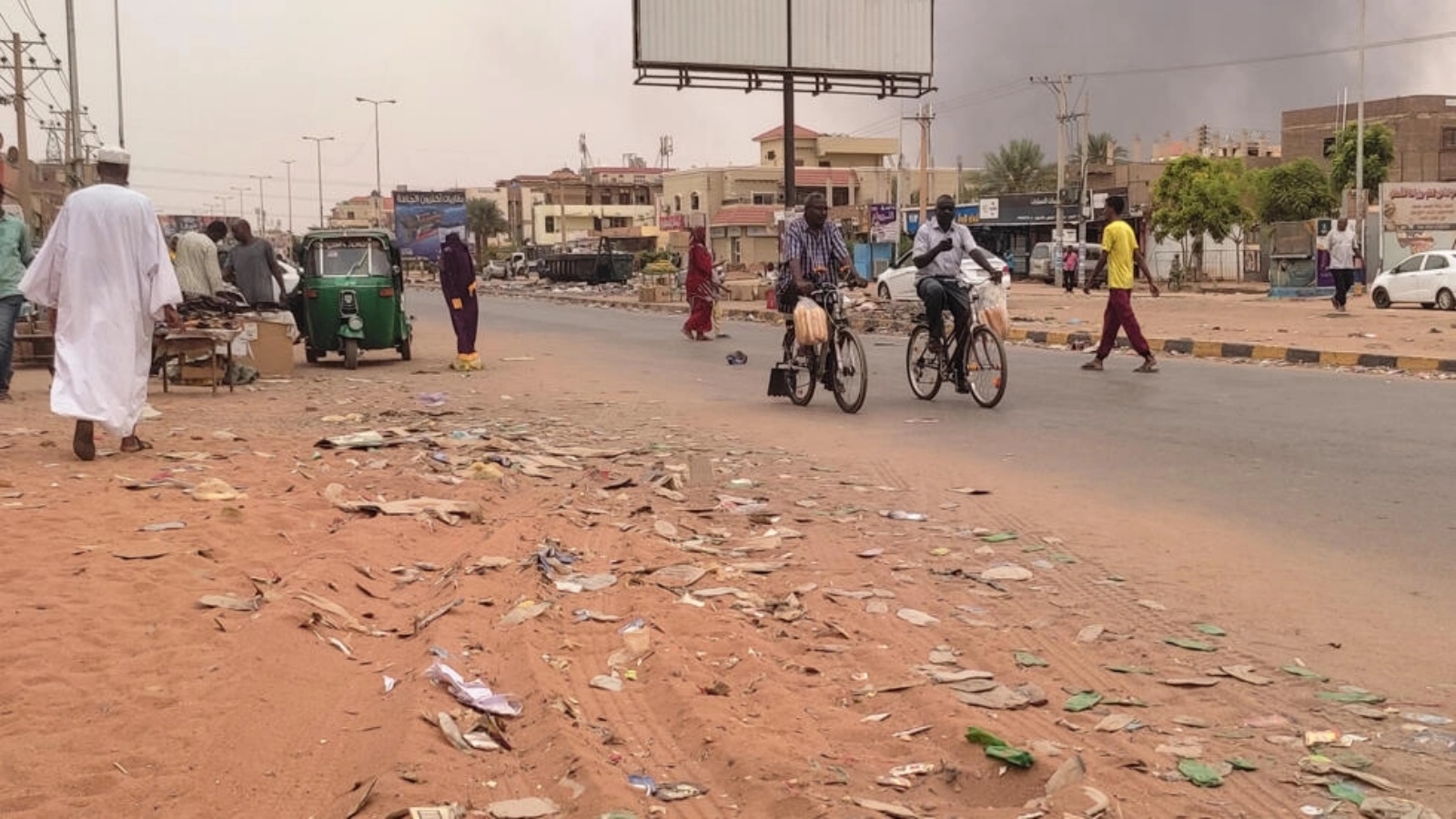 يعبرون احد شوارع ام درمان السودانية فيما دخان المعارك يتصاعد فوق المباني في 15 يوليو 2023