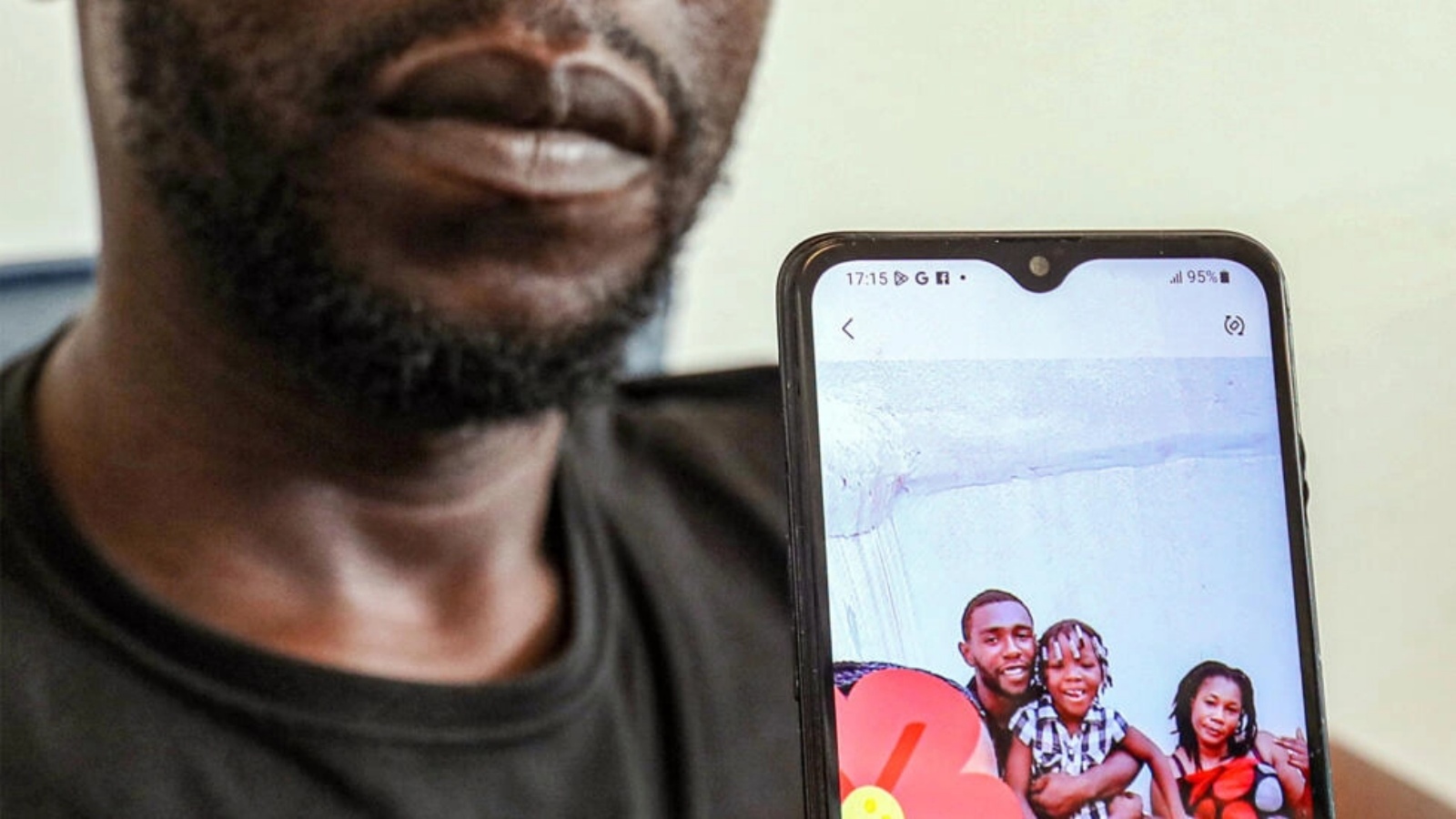 باتو المهاجر من الكاميرون يحمل هاتفه النقال وعليه صورة له مع زوجته وابنتهما اللتين توفيتا خلال محاولة لعبور الصحراء من تونس إلى ليبيا، خلال مقابلة أجرتها معه وكالة فرانس برس في موقع لم يُكشف عنه قرب العاصمة الليبية طرابلس في 2 أغسطس 2023