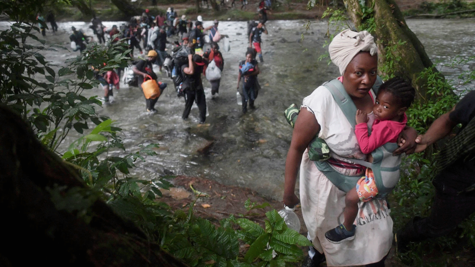 امرأة من هايتي تحمل طفلًا صغيرًا وهي تعبر جزءًا من Darien Gap ، بالقرب من Acandi ، كولومبيا في عام 2021