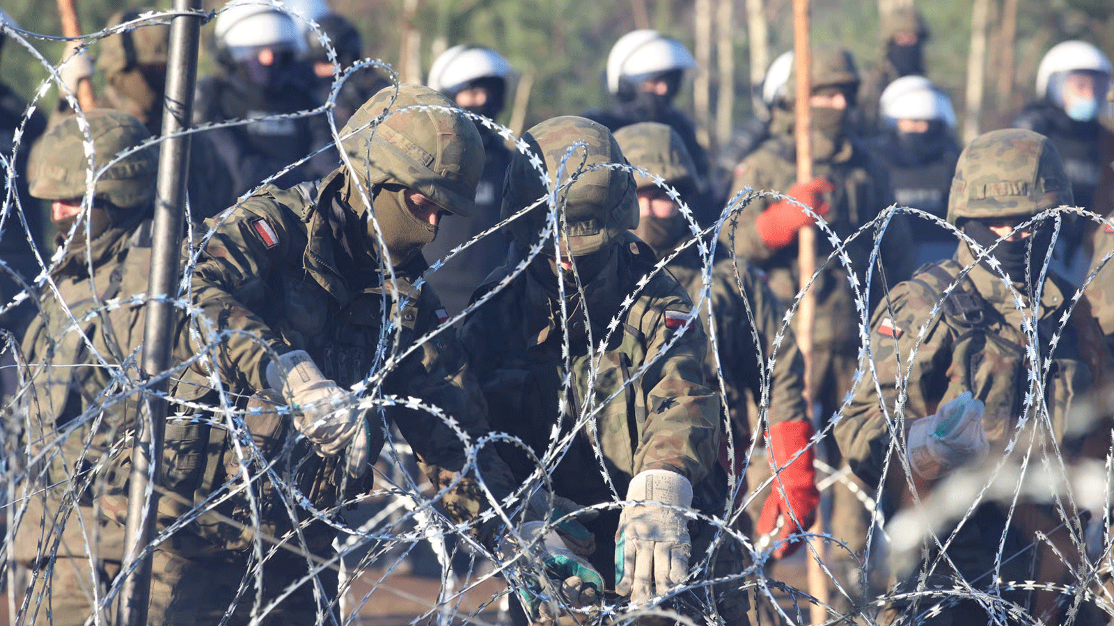 أفراد الأمن البولنديون وراء سياج من الأسلاك الشائكة على الحدود البيلاروسية البولندية حيث تجمع آلاف المهاجرين بهدف دخول بولندا
