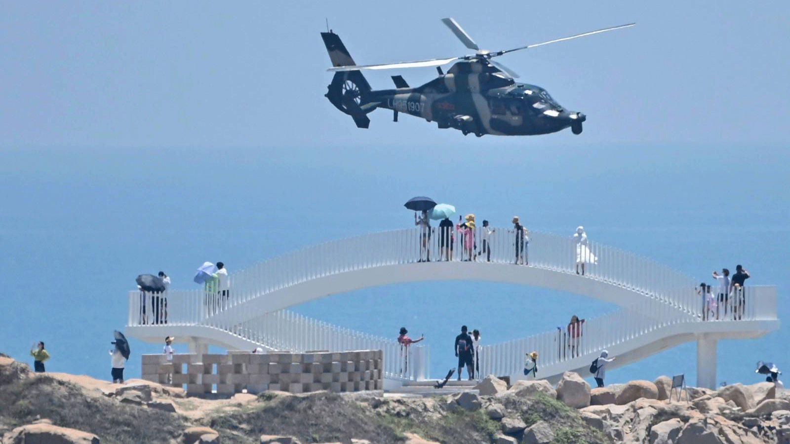 السائحون ينظرون إلى طائرة هليكوبتر عسكرية صينية تحلق فوق جزيرة بينغتان، إحدى أقرب النقاط في البر الرئيسي الصيني لتايوان، في مقاطعة فوجيان، قببل مناورات عسكرية ضخمة قبالة تايوان