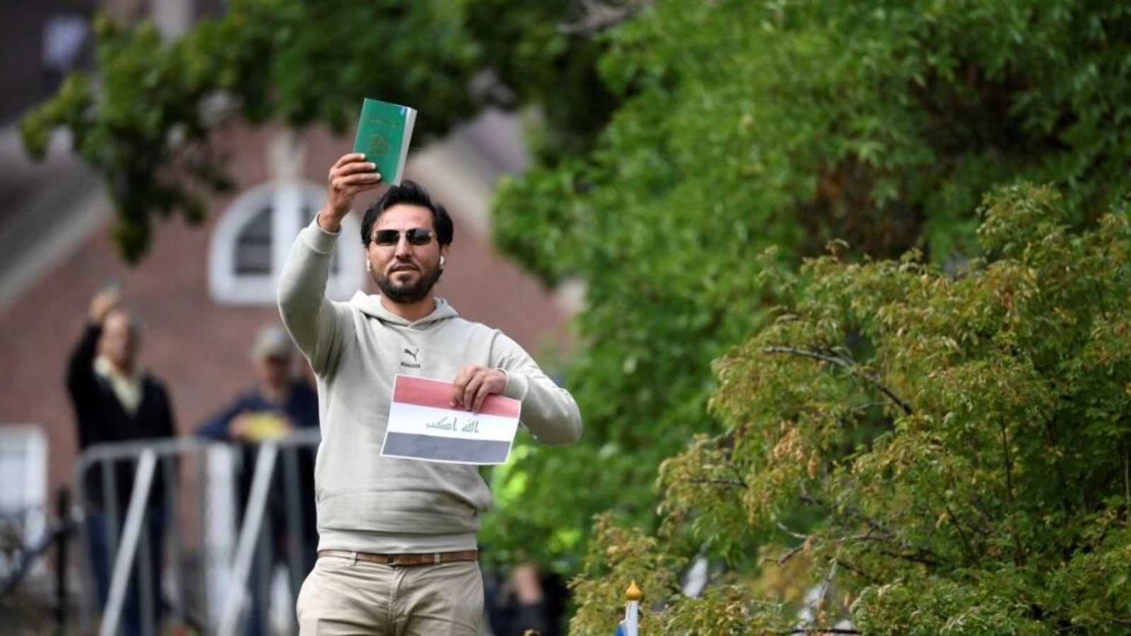 المتظاهر سلوان موميكا يحمل المصحف وورقة عليها علم العراق أثناء احتجاج خارج السفارة العراقية في ستوكهولم، السويد، في 20 يوليو 2023