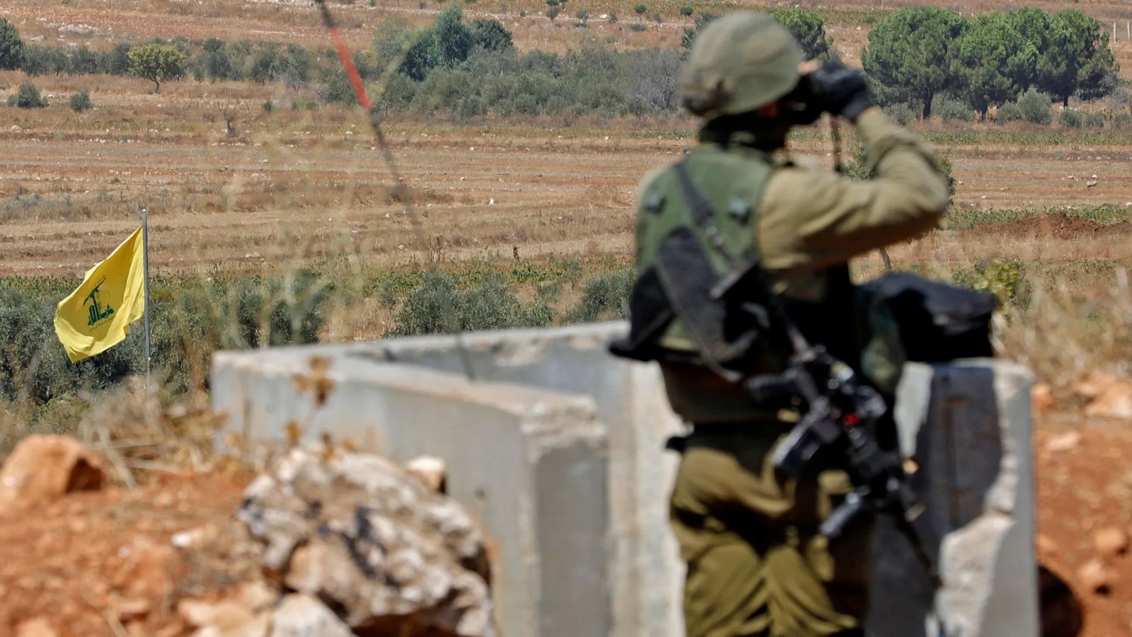 جنود إسرائيليون يقفون في شمال إسرائيل على طول الحدود مع لبنان بالقرب من علم حزب الله (أرشيفية)