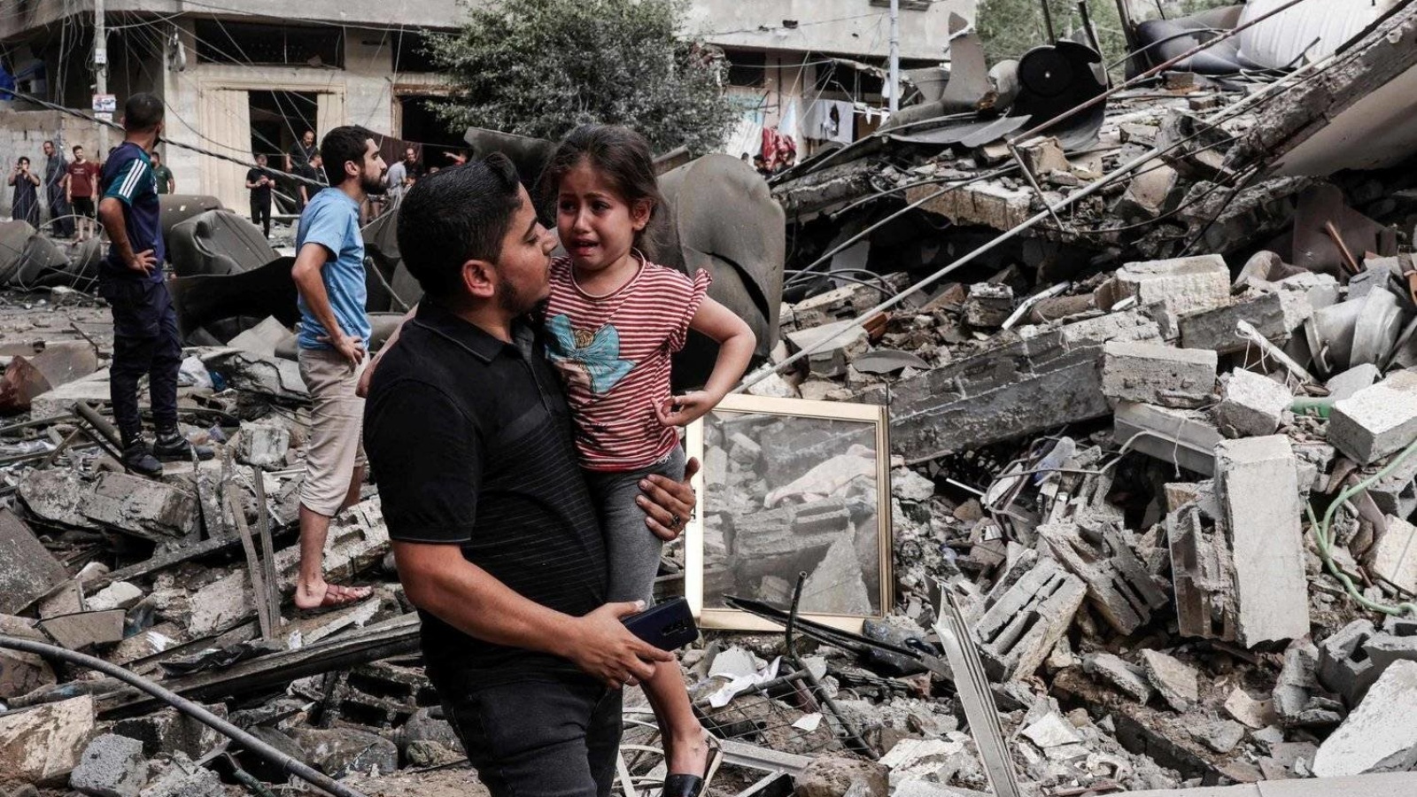 رجل يحمل طفلة باكية أمام مبنى دمرته غارة إسرائيلية على قطاع غزة 