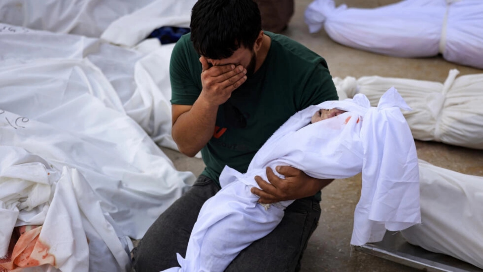 رجل يبكي وهو يحمل جثة طفله الملفوف بكفن أمام مشرحة مستشفى الأقصى في دير البلح في وسط قطاع غزة بعد غارة إسرائيلية في 22 أكتوبر 2023 