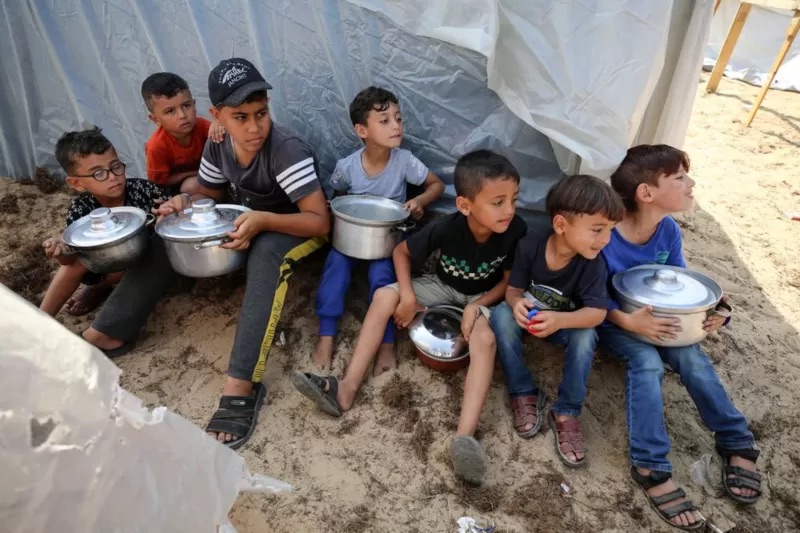 أطفال فلسطينيون بقطاع غزة يجلسون في انتظار الطعام بين مخيمات الأونروا في 24 أكتوبر/تشرين الأول