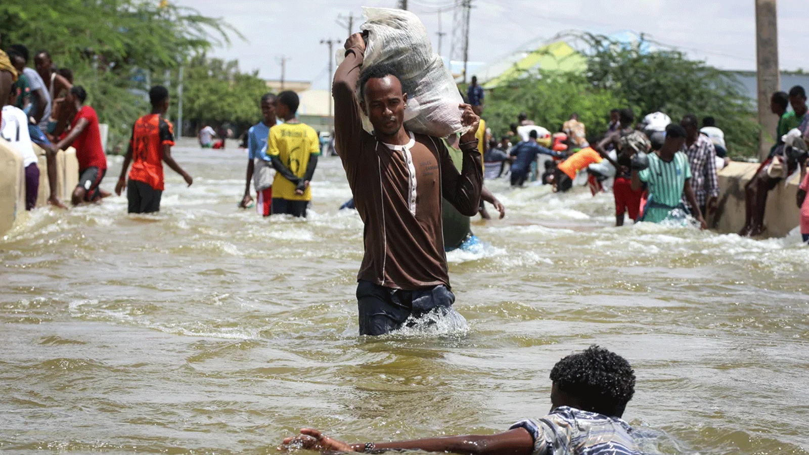 رجل يحمل كيسًا وسط مياه الفيضانات في بلدوين، وسط الصومال