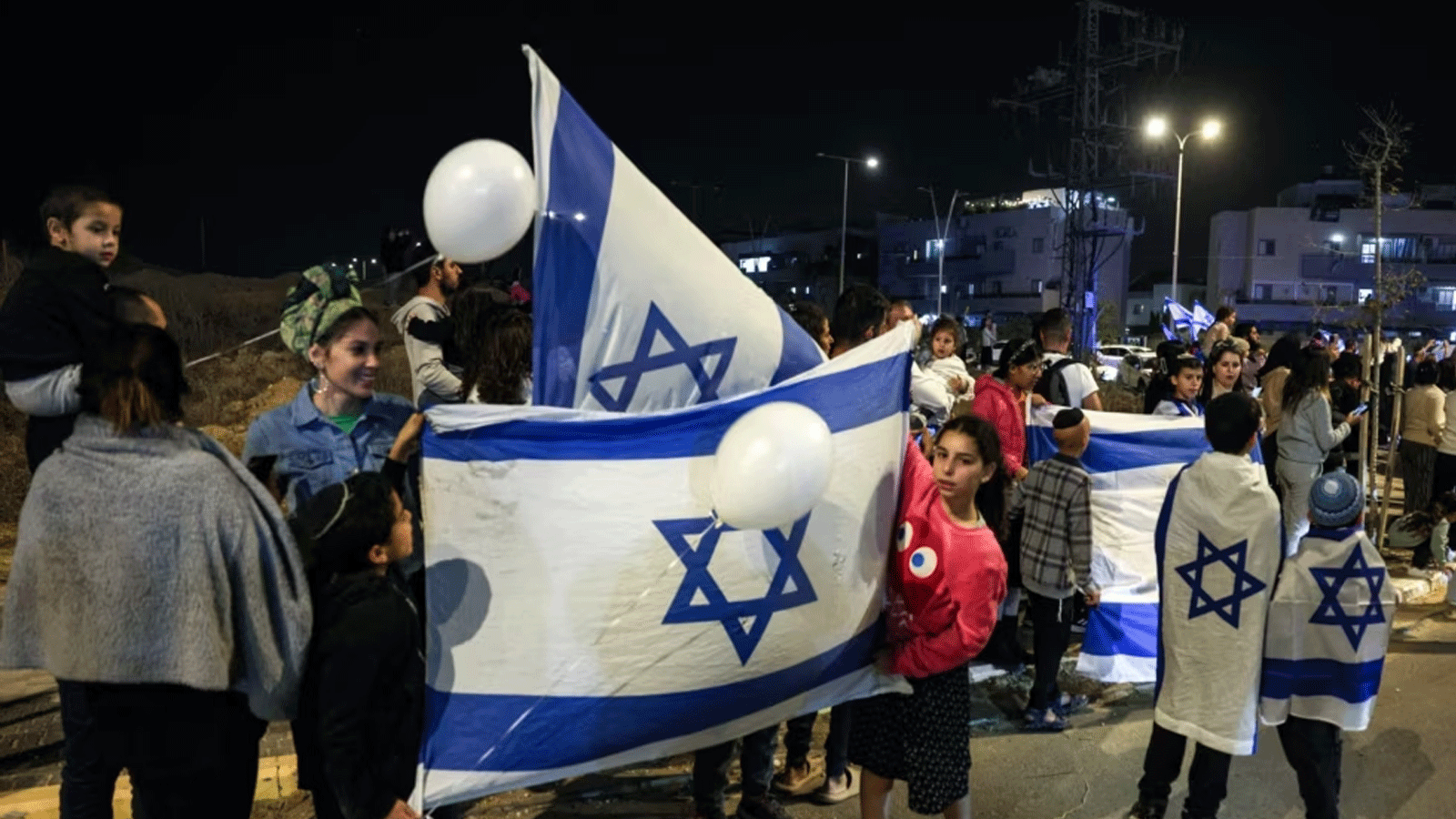 أشخاص يحملون أعلام إسرائيل ويهتفون بعد مرور مركبة تقل رهائن أطلقتهم حماس باتجاه قاعدة عسكرية في أوفاكيم، جنوب إسرائيل، في 26 نوفمبر(تشرين الثاني) 2023