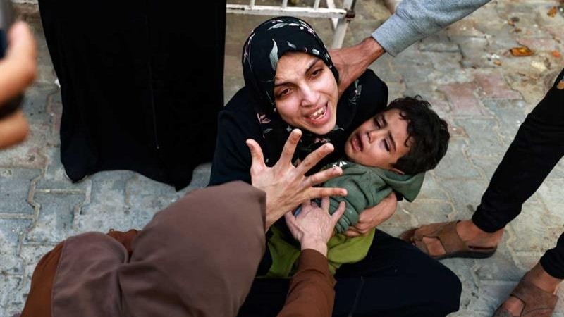امرأة تحمل طفلاً تبكي على طفلتها التي قُتلت في غارة إسرائيلية في رفح بجنوب قطاع غزة، بينما تنتظر استلام الجثة لدفنها في باحة مستشفى النجار في 1 ديسمبر 2023