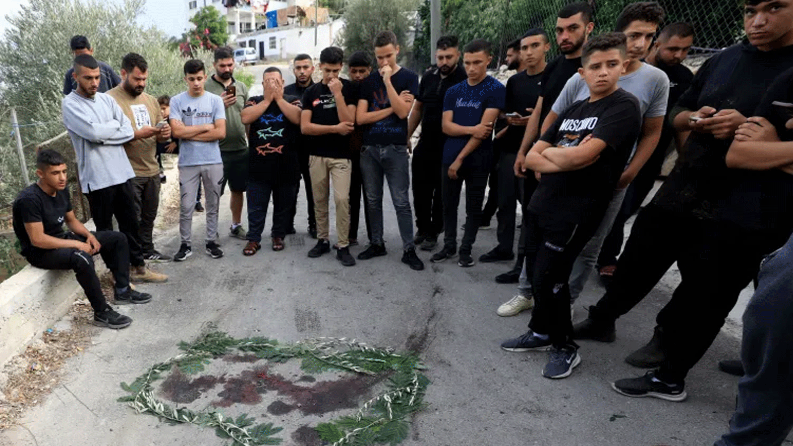 أشخاص يتجمعون حول بقعة دم محاطة بأوراق الشجر بالقرب من مدينة طولكرم بالضفة الغربية، حيث قُتل فلسطينيان خلال اشتباكات مع القوات الإسرائيلية