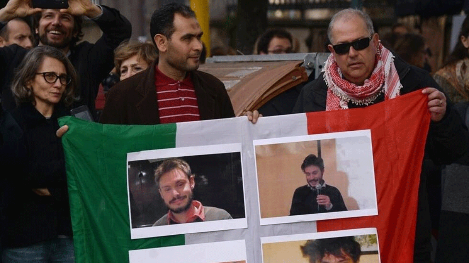 أشخاص يحملون علمًا إيطاليًا عليه صور جوليو ريجيني، طالب الدكتوراه الذي عُثِرَ عليه ميتًا وعليه آثار تعذيب بعد اختفائه في القاهرة، خلال مظاهرة أمام السفارة المصرية في روما