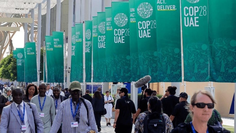 مشاركون في مؤتمر كوب 28 المناخي بدبي يسيرون أمام لافتات خاصة بالمؤتمر في 3 ديسمبر 2023