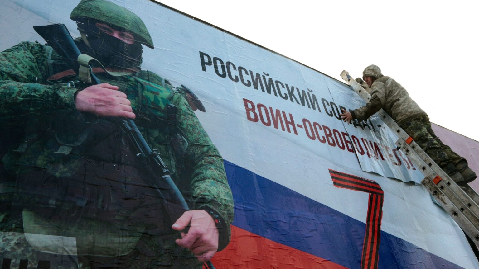 صورة من ألأرشيف لرجل يلصق لافتة ضخمة عليها صورة جندي روسي ومكتوب عليها 