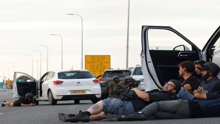 صحفيون يختبئون خلف السيارات بينما يتخذ جنود إسرائيليون مواقعهم خلال اشتباكات مع مقاتلين فلسطينيين قرب كيبوتس غيفيم، على الحدود مع غزة، في 7 أكتوبر 2023