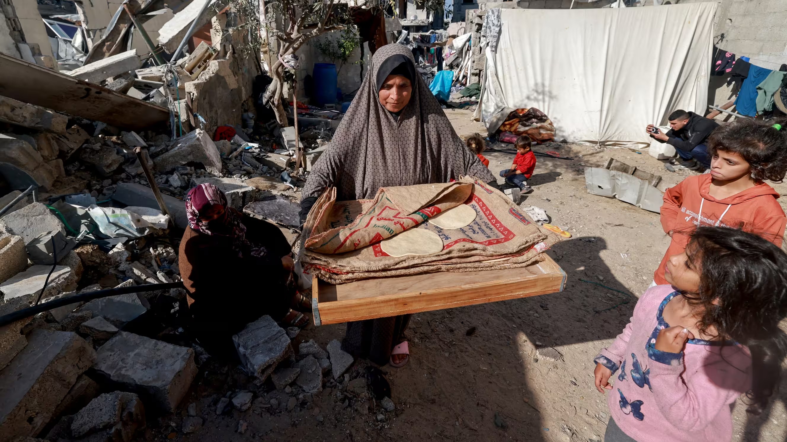 امرأة تحمل الخبز بجوار المنازل المدمرة في رفح، جنوب قطاع غزة، 11 ديسمبر 2023