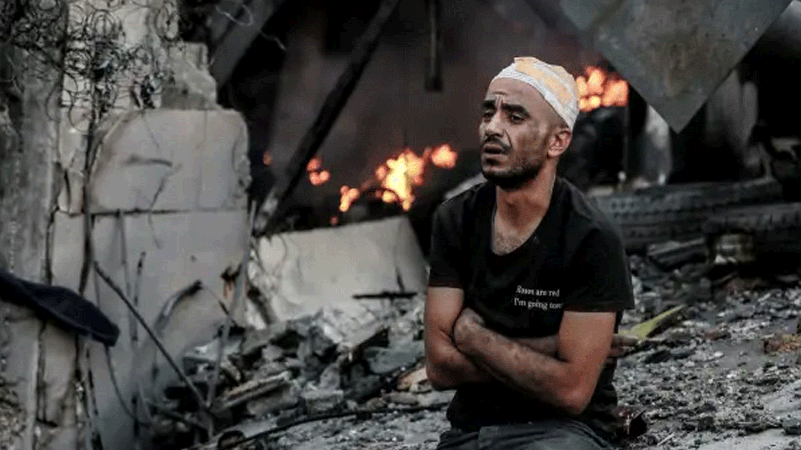 رجلٌ مصاب يجلس أمام مبنى مشتعل في أعقاب غارة إسرائيلية على مدينة غزة