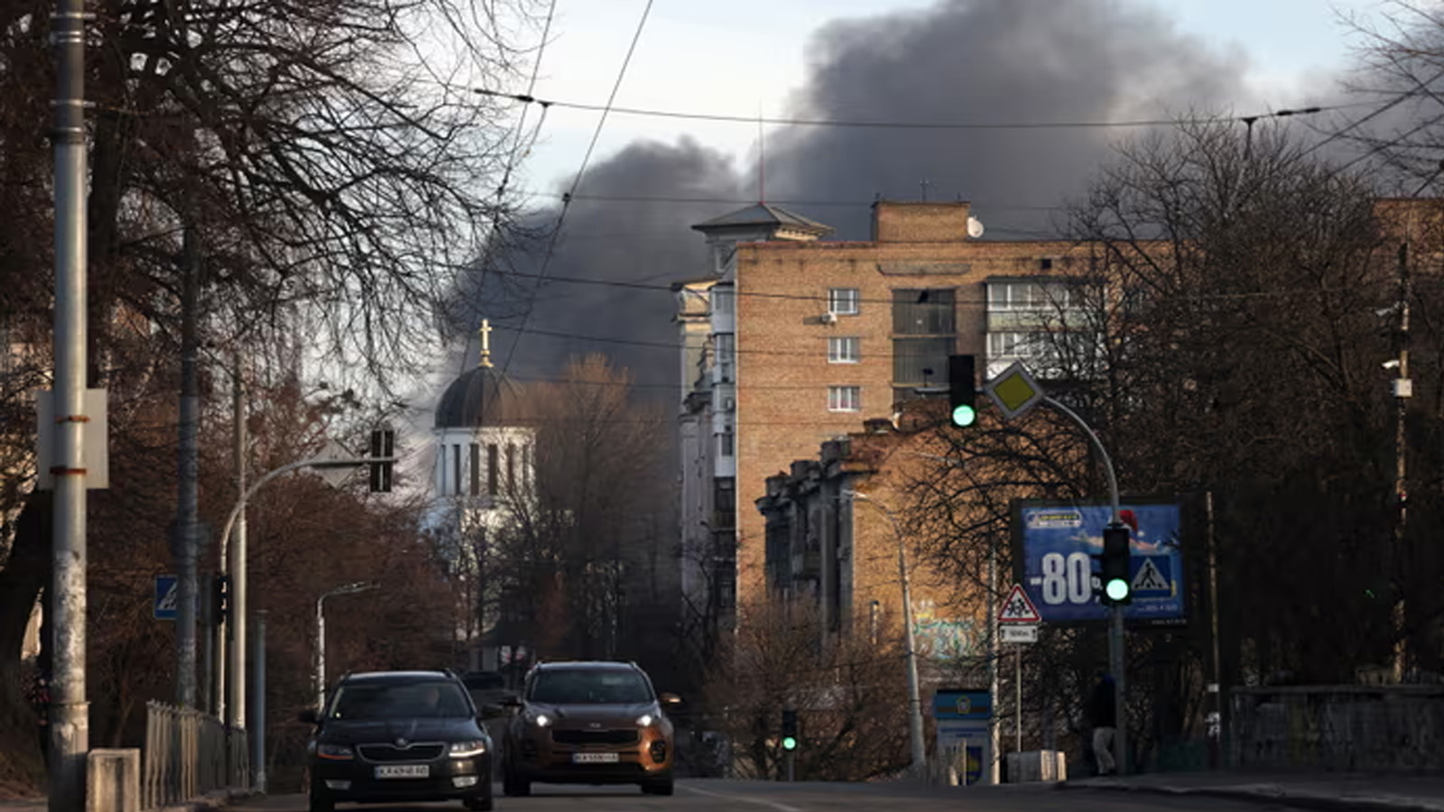 سيارات تسير في الشارع بينما يتصاعد الدخان من حريق بعد هجوم صاروخي في وسط كييف