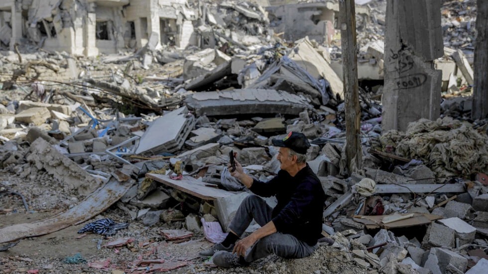 فلسطيني يستخدم هاتفه فيما يجلس وسط ركام المباني المدمّرة في مدينة غزة بتاريخ 25 تشرين الثاني/نوفمبر 2023