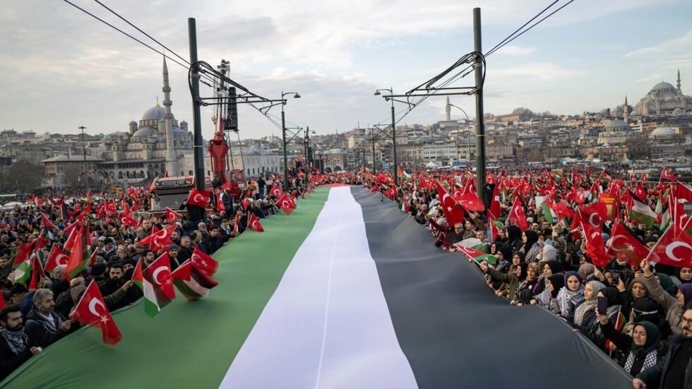 آلاف المتظاهرين ينشرون علما فلسطينيا ضخما تضامنا مع قطاع غزة في ظل الحرب بين إسرائيل وحماس، خلال تظاهرة فوق جسر غلطة في اسطنبول في الأول من كانون الثاني/يناير 2024