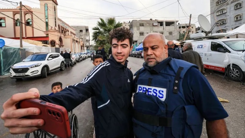 MAHMUD HAMS/AFP | شاب فلسطيني يلتقط صورة مع وائل الدحدوح خلال تغطيته للأحداث في رفح