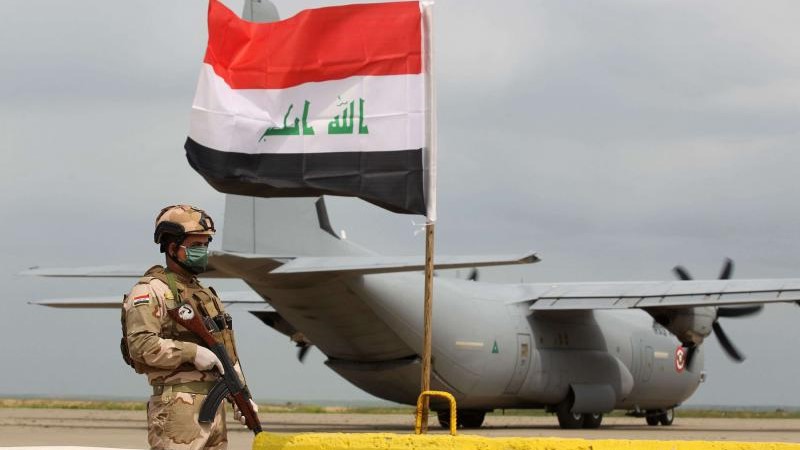 جندي عراقي يقف أمام حاملة طائرات عسكرية أمريكية في قاعدة القيارة الجوية بالعراق