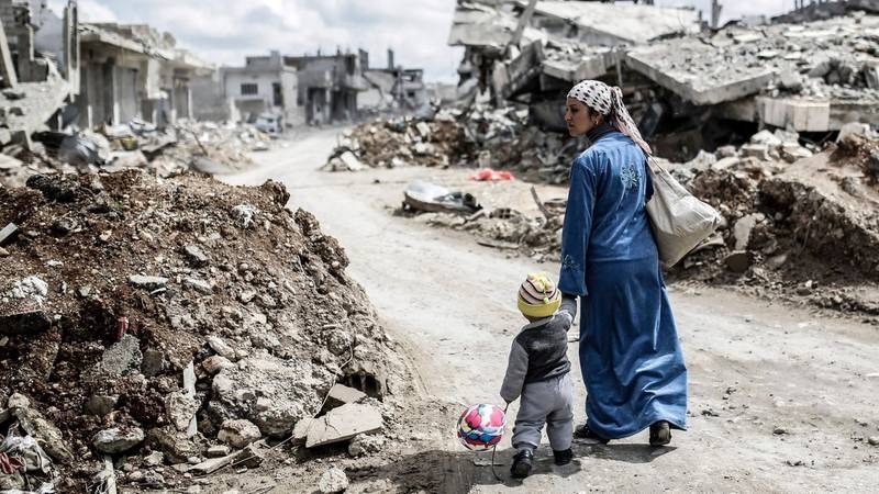 سورية وابنها بين المباني المدمرة في قرية الطفيل الحدودية بفعل الحرب السورية وقصف حزب الله على مواقع المعارضة في عام 2013