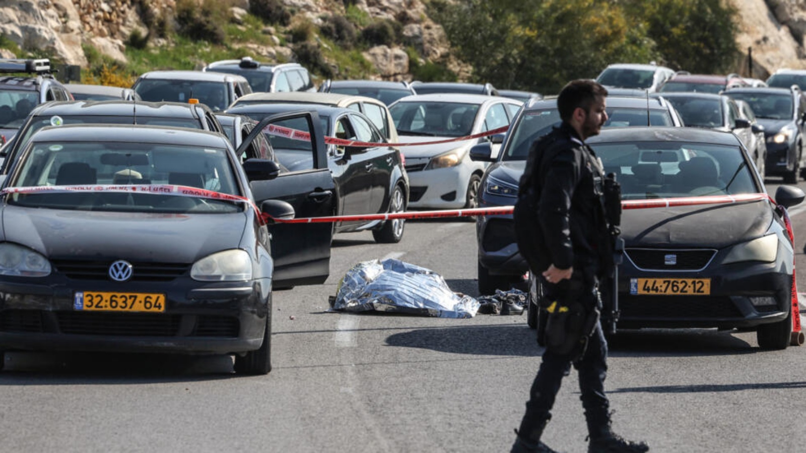 عنصر من قوات الأمن الإسرائيلية يسير قرب جثة ملقاة على الأرض وسط مركبات قرب مستوطنة معالية أدوميم شرق القدس في 22 شباط (فبراير) 2024 بعد هجوم نفذه ثلاثة فلسطينيين 