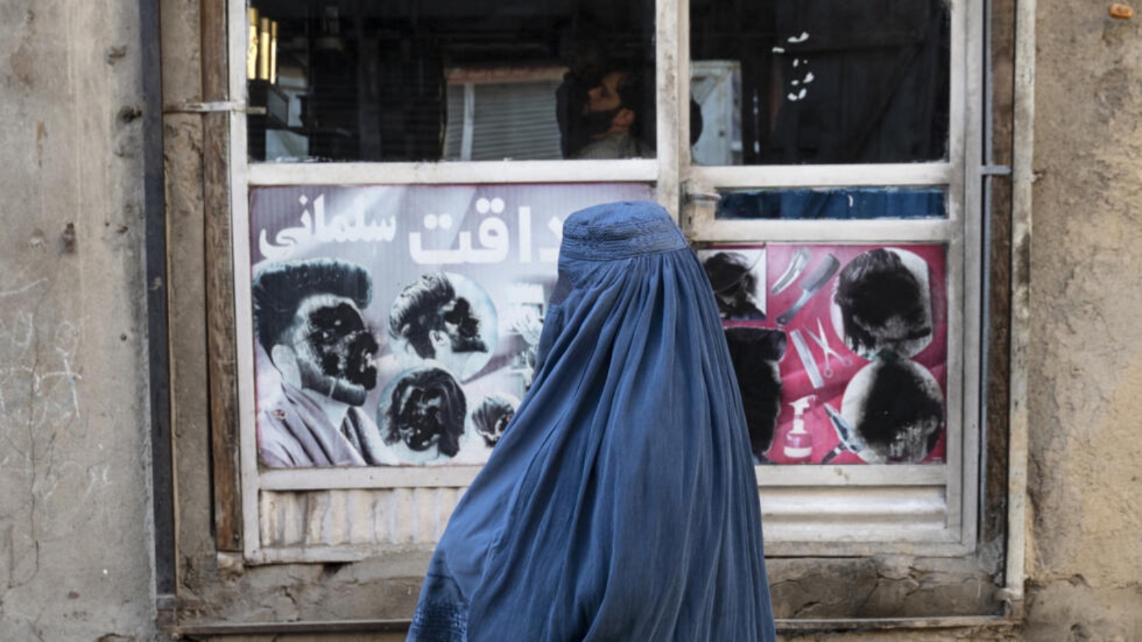 امرأة أفغانية ترتدي البرقع تمر أمام محل حلاقة في كابول في 31 كانون الثاني (يناير) 2024 