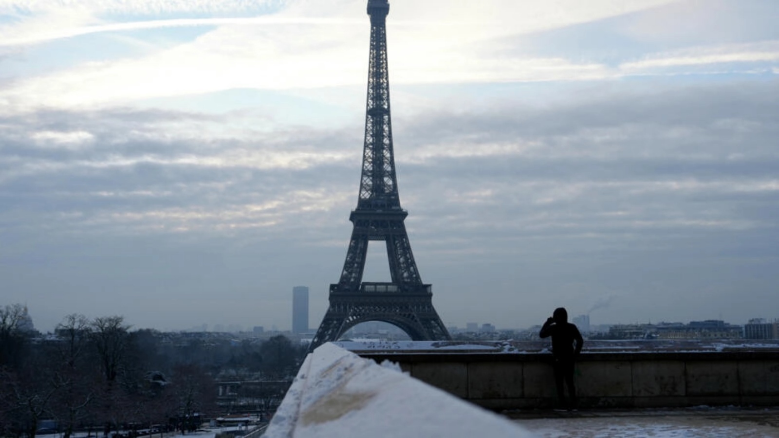 أحد المشاة ينظر إلى برج ايفل تحت الثلج في باريس في 18 كانون الثاني (يناير) 2024 